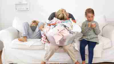 Overwhelmed mother with ADHD buries her head in a full laundry basket, struggling to reframe negative thoughts and gender roles.