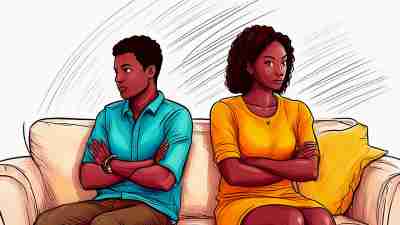 A male/ female couple sit on couch with arts crossed, facing away from each other, communicating hurt feelings.